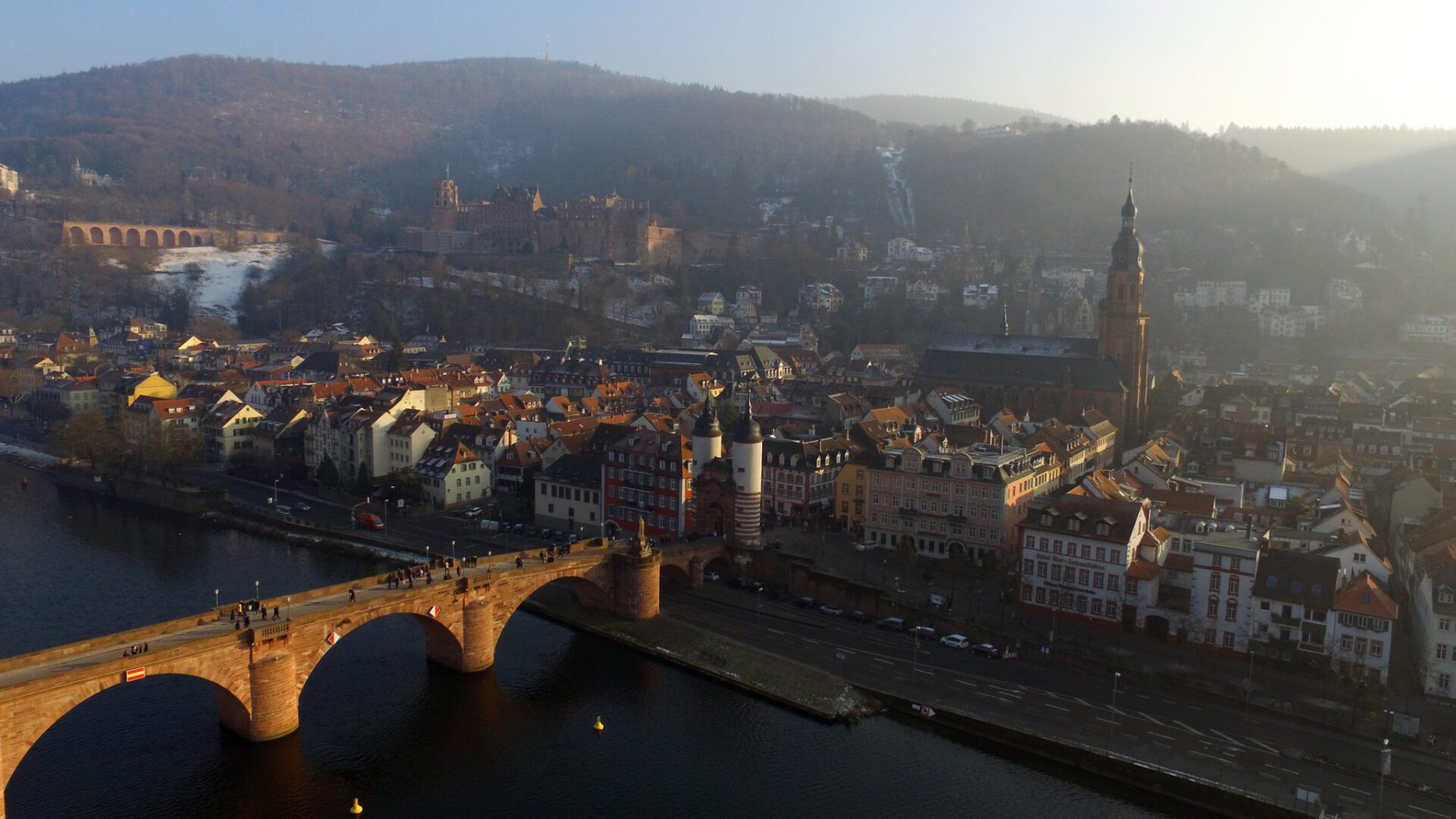 Luftbild von Heidelberg: Meine Drohne schwebt kurz nach Sonnenaufgang über dem Neckar. Links im Bild ist die alte Brücke zu sehen, die von der Sonne beleuchtet wird.