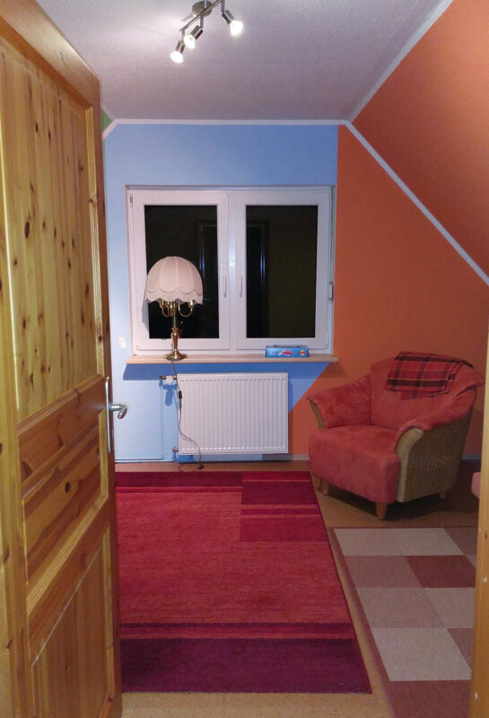 Blick von der Zimmertür zur Fensterseite des Streamzimmers. Man sieht rot, blau und grün als Wandfarbe