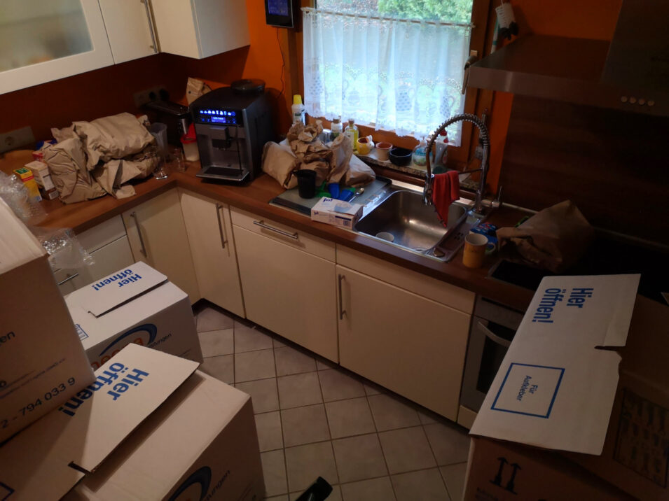 Foto der kleinen Küche, die mit Kisten und Geräten vollgestellt ist.