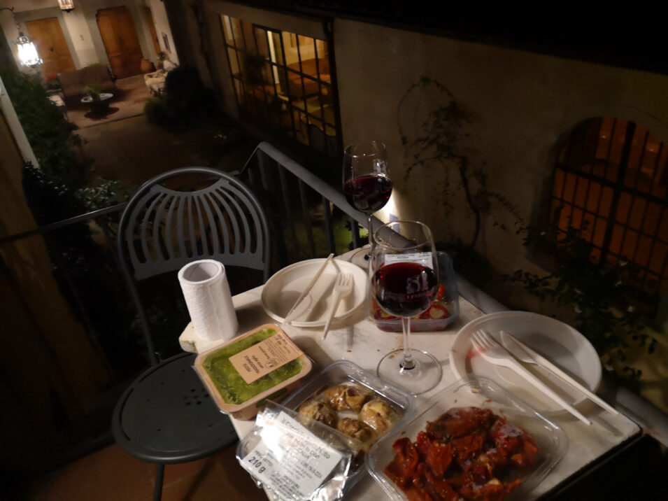 Balkontisch mit kompostierbarem Geschirr, zwei Gläsern Wein und Antipasti-Packungen