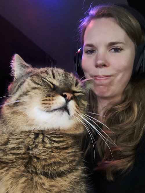 Lucyda mit Kater Lopi auf dem Schoß. Lucyda schaut doof grinsend in die Kamera, Lopi hat die Augen geschlossen und sieht flauschig aus