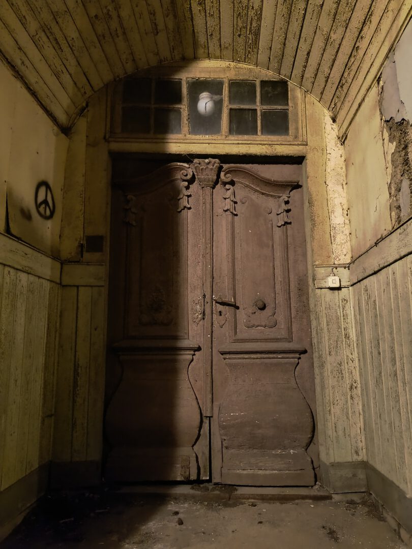 Das Haus hat einen tiefen Hauseingang. Eine zweiflügelige Holztür mit Schnitzereien führt ins Haus. Die Seiten des Eingangs sind mit Holz vertäfelt, ein Tonnengewölbe schließt nach oben ab.