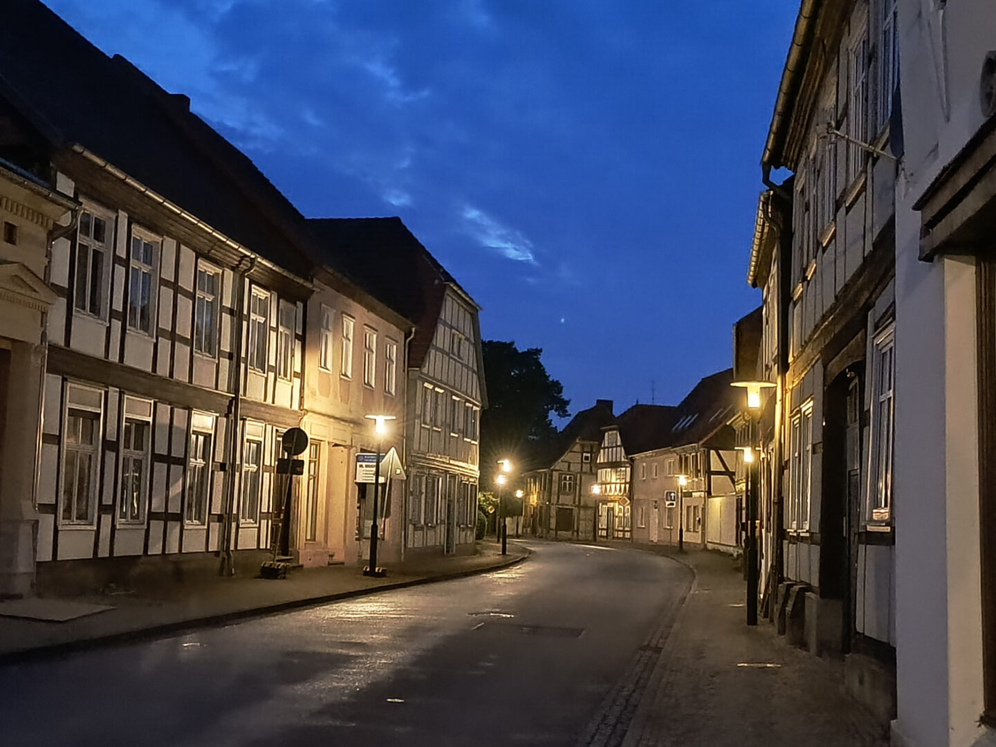 Gelb leuchtende Straßenlampen erhellen eine Straße mit Fachwerkhäusern. Keine Autos weit und breit, auch nicht am Straßenrand.