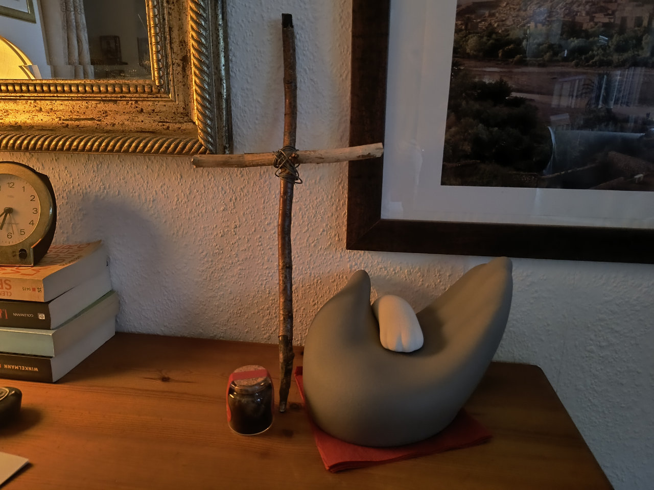 Eine Urne in Form einer stilisierten, geöffneten Hand und einer darauf liegenden Pfote steht neben einem einfachen Holzkreuz aus zwei mit Drähten geformten Stöckchen aus dem Wald. Daneben eine kleine Glasflasche, die dunkles Fell enthält.
