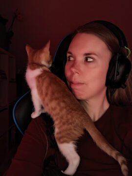 Eine rot-weiße kleine Katze stützt sich mit zwei Vorderpfoten auf meiner Schulter und schaut nach oben.